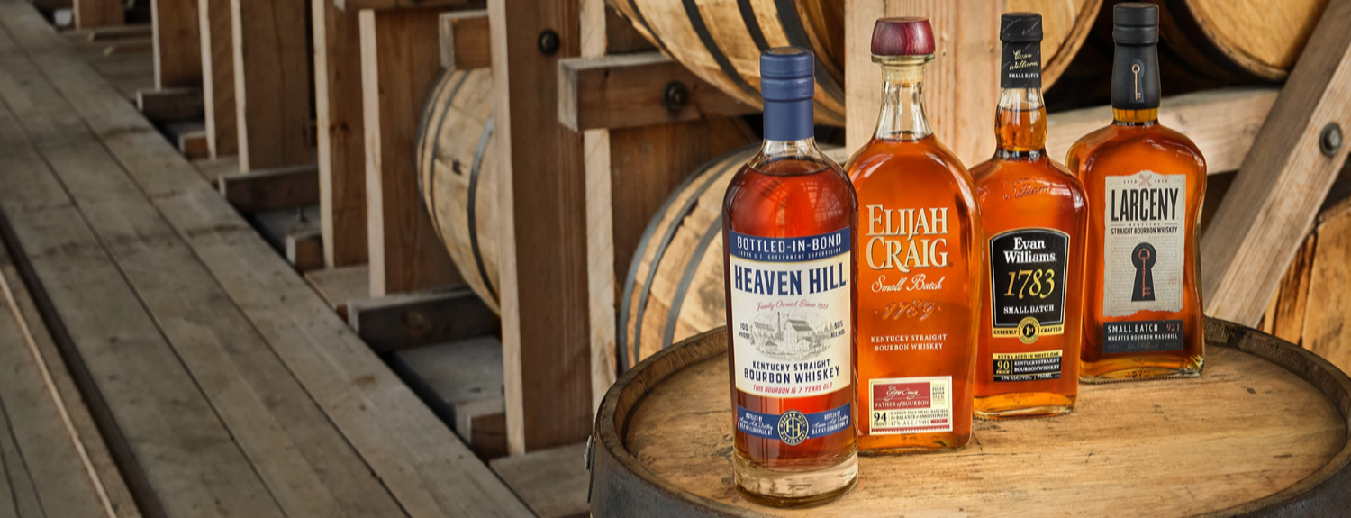 Four bottles of Heaven Hill bourbon on a wooden barrel with barrels in the background.
