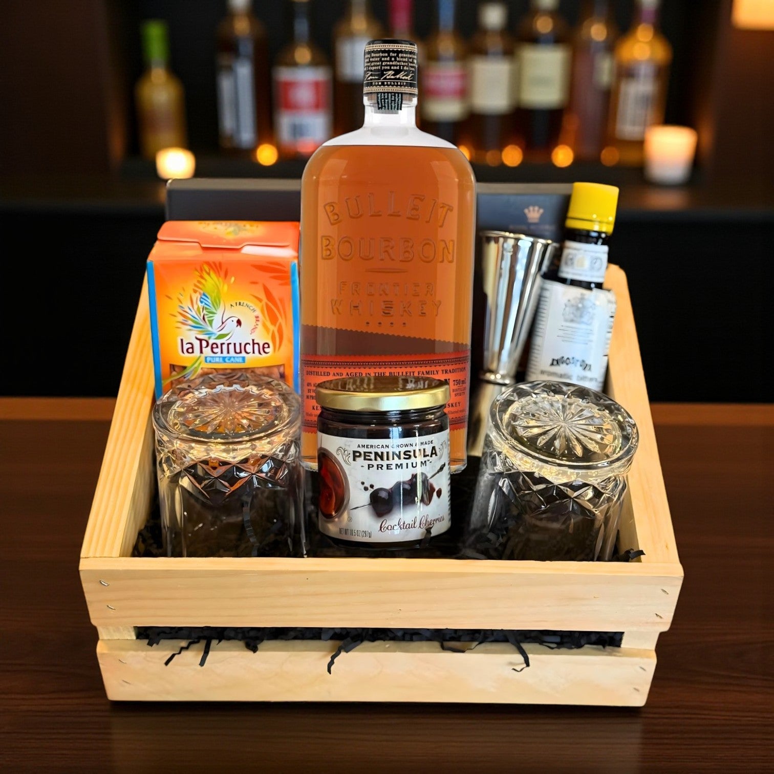 Bulleit Bourbon Old Fashioned Gift Crate with whiskey, bar tools, cherries, bitters, and glasses displayed on wooden bar – lifestyle photo from Total Bourbon
