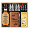 The Balvenie 14 Year Caribbean Cask Single Malt Scotch Whisky gift crate top-down view featuring 750ml bottle, two old-fashioned crystal-cut whiskey glasses, Royal Reserve Whiskey Stones set, Brilliant Ideas leather bourbon journal with wooden pen, and Ferrero Rocher 8-piece gold bag in wooden crate with black crinkle paper on white background.