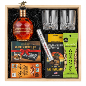 Blanton's Gold Edition Single Barrel Bourbon 700ml gift crate with gold horse stopper, crystal-cut old fashioned glasses, Royal Reserve whiskey stones set with tray, Montecristo Platinum cigar tube, Black Rifle Coffee Tactisquatch blend, Chocolove Almonds & Sea Salt dark chocolate bar, and Wonderful Pistachios in black crinkle paper on white background