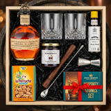 Blanton's Old-Fashioned cocktail gift crate with Blanton's Original bourbon, crystal glasses, bitters, muddler, bar spoon, jigger, cocktail cherries, sugar cubes, and whiskey stones nestled in black zigzag crinkle paper inside wooden crate on rustic aged oak surface with warm amber bourbon bar lighting