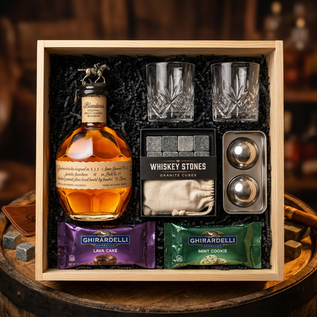 Blanton's Original Single Barrel Bourbon gift crate with iconic horse stopper, crystal-cut old fashioned glasses, premium whiskey stones gift set, XXL stainless steel whiskey balls, and Ghirardelli chocolates on rustic aged oak surface with warm amber bourbon bar lighting and moody bokeh