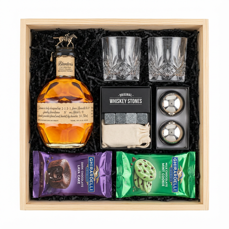 Blanton's Original Single Barrel Bourbon gift crate with iconic horse stopper, crystal-cut old fashioned glasses, premium whiskey stones gift set, XXL stainless steel whiskey balls with freezer tray, Ghirardelli Dark Chocolate Lava Cake, and Ghirardelli Milk Chocolate Mint Cookie in black crinkle paper on white background