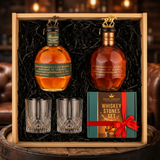Blanton's Special Reserve Green Label 700ml and Blanton's Gold Edition 700ml dual-bottle gift crate with bronze and gold horse stoppers, crystal-cut old fashioned glasses, and Royal Reserve whiskey stones gift box nestled in black crinkle paper inside wooden crate on rustic aged oak surface with warm amber bourbon bar lighting