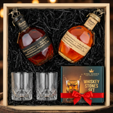 Blanton's Takara Black Edition and Blanton's Takara Red Edition dual-bottle gift crate with bronze horse stoppers and Japanese labels, crystal-cut old fashioned glasses, and Royal Reserve whiskey stones gift box nestled in black zigzag crinkle paper inside wooden crate on rustic aged oak surface with warm amber bourbon bar lighting
