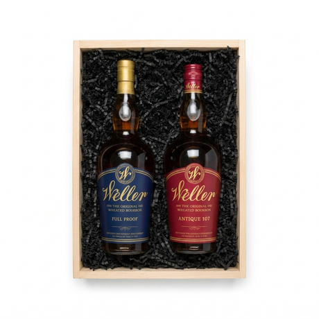 A wooden gift box filled with black crinkle paper packaging, holding two bottles of Weller whiskey. The left bottle has a blue label and a gold cap, and the right bottle has a red label and a red cap.
