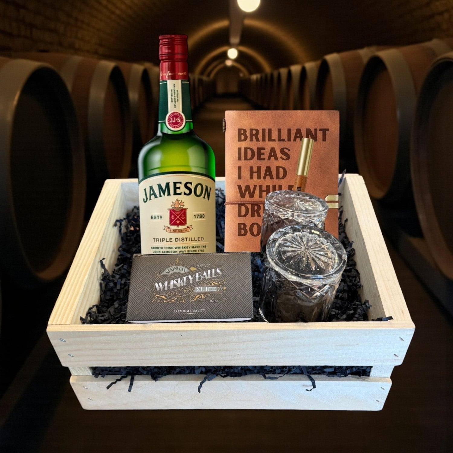Jameson Irish Whiskey Gift Crate with bottle, glasses, journal, and whiskey balls displayed in a wooden crate against a warm barrel room backdrop – premium Irish whiskey gift from Total Bourbon