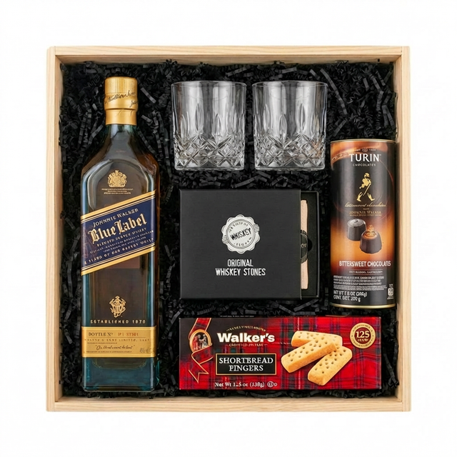 Johnnie Walker Blue Label Scotch Gift Crate featuring a 750ml bottle, two crystal cut whiskey glasses, Original Whiskey Stones set, Walker's Shortbread Fingers, and Turin Johnnie Walker Bittersweet Chocolates tube, arranged in a light wooden gift box with black crinkle paper