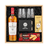 The Macallan 12 Year Sherry Oak Single Malt Scotch gift crate, crystal-cut old fashioned glasses, premium whiskey stones gift set, Ferrero Rocher chocolates, and Walker's shortbread fingers in black crinkle paper on white background