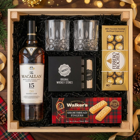 Bird's eye view of The Macallan 15 Year Old Double Cask Single Malt Scotch gift crate with crystal-cut old fashioned glasses, premium whiskey stones gift set, Ferrero Rocher chocolates, and Walker's shortbread fingers on elegant dark wood surface with warm golden bokeh lights and holiday decor