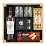 The Macallan 15 Year Old Double Cask Single Malt Scotch gift crate with crystal-cut old fashioned glasses, premium whiskey stones gift set, Ferrero Rocher chocolates, and Walker's shortbread fingers in black crinkle paper on white background