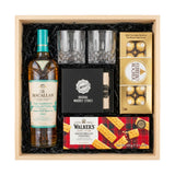 The Macallan Harmony Collection Phoenix Honey Orchid Tea Jing gift crate with crystal-cut old fashioned glasses, premium whiskey stones gift set, Ferrero Rocher chocolates, and Walker's shortbread fingers laying flat in black crinkle paper on white background