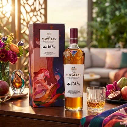 The Macallan Litha Highland Single Malt Scotch Whisky lifestyle scene featuring bottle with burgundy cap and brushstroke Litha label alongside colorful artistic presentation box with flowing peacock and strawberry design in burgundy, purple, pink and teal, displayed with crystal whisky glass on polished surface with warm summer golden hour lighting.