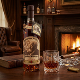 Pappy Van Winkle's Family Reserve 23 Year Old Kentucky Straight Bourbon Whiskey Limited Edition lifestyle scene featuring bottle with dark brown wax top, vintage sepia portrait label, and black Limited Edition hang tag, displayed with crystal bourbon glass on rich dark wood surface in ultra-luxurious bourbon den setting with warm ambient fireplace lighting.